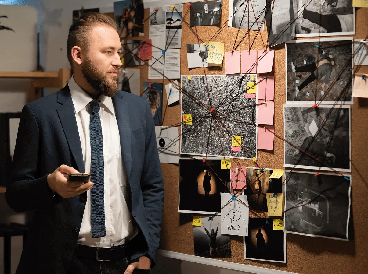 A man in a suit standing next to a wall covered with photos.